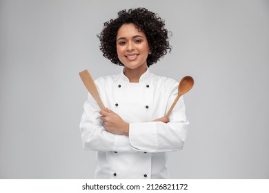 cooking, culinary and people concept - happy smiling female chef in white jacket with wooden spoon and spatula over grey background - Powered by Shutterstock