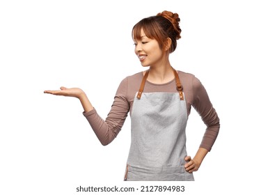 cooking, culinary and people concept - happy smiling female chef or waitress in apron holding something imaginary on her hand over white background