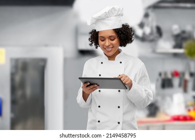 cooking, culinary and people concept - happy smiling female chef in toque and jacket with tablet pc computer over restaurant kitchen background
