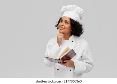 Kochen, Gastronomie- und People-Konzept - glücklicher, lächelnder Küchenchef in weißer Toque und Jacke mit Lesebuch auf grauem Hintergrund