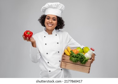 Cooking, Culinary And People Concept - Happy Smiling Female Chef In Toque Holding Food In Wooden Box And Red Pepper Over Grey Background