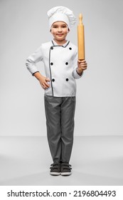 Cooking, Culinary And Profession Concept - Happy Smiling Little Boy In Chef's Toque And Jacket With Rolling Pin Over Grey Background