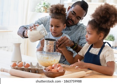 Cooking with daddy. Caring concentrated african foster father teaching two focused interested adopted children siblings little brother and older sister sift flour for mixing dough and baking home cake - Powered by Shutterstock