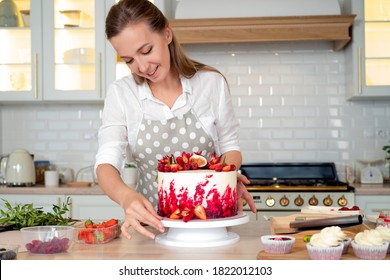 cooking and decoration of cake with cream. Young woman pastry chef in the kitchen decorating red velvet cake. Happy woman in apron in kitchen makes beautiful birthday cake, cooking and pastry skills - Powered by Shutterstock