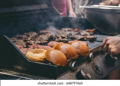 Cooking delicious juicy meat burgers and buns on the grill outdoor. Selective focus