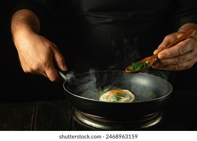 Cooking delicious scrambled eggs in the kitchen. A chef adds a spoonful of dill to a hot pan of eggs while preparing a vegetarian meal. - Powered by Shutterstock