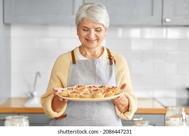 cooking food, baking and culinary concept - happy smiling senior woman holding big plate with cupcakes on kitchen at home - Powered by Shutterstock