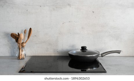 Cooking Food Concept. Panoramic View Of Frying Pan On Glass Ceramic Stove Standing Against Grey Copy Space Wall Near Wooden Spoons. Modern Kitchen With Built In Appliance And Marble Countertop