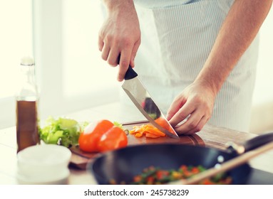 cooking, food and home concept - close up of male hand cutting pepper on cutting board at home