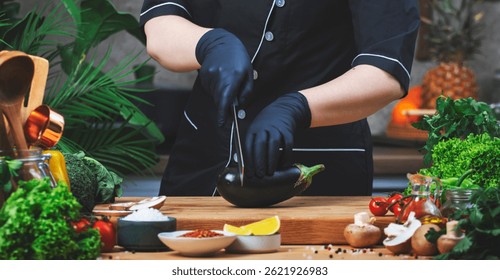 Cocinar comida en la cocina.  Chef corta berenjena fresca Mesa de madera, utensilios de cocina, verduras, hierbas e ingredientes. Comida vegana saludable, recetas, blogueo