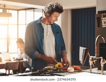 Cooking, food and man cutting vegetables in the kitchen for diet, healthy or nutrition dinner. Recipe, book and mature male person from Canada chop ingredients for a supper or lunch meal at home. - Powered by Shutterstock