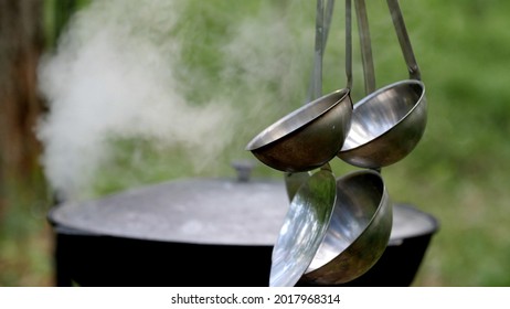 Cooking food on the hike. Ladles hang next to the pan. Close up. Saucepan with food is on the metal stove in nature on the background. White steam rises into the air. Makeshift kitchen in the forest.