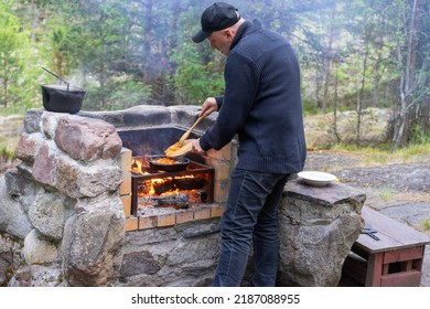 Cooking food on outdoor grill. Man prepares food on fire. Adult man is preparing dinner. Stone grill place in picturesque location. Cooking during country holiday. Cooking in stone open oven