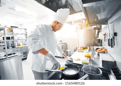 cuisine, profession et concept de personnes - chef masculin heureux cuisinier cuisinier mâle qui verse de l'huile à la poêle à la cuisine du restaurant