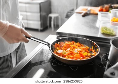 cooking food, profession and people concept - close up of male chef with frying pan stewing vegetables at restaurant kitchen