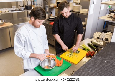 cooking food, profession and people concept - happy male chef cook with knife peeling carrot and chopping cucumber on cutting board at restaurant kitchen - Powered by Shutterstock