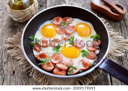 Cooking fried eggs with sausages and fresh parsley.