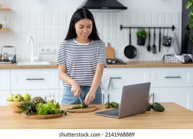 Cooking Healthy Food Concept. Young Asian Woman Watching Recipe Online Using Laptop Computer While Standing At Home Kitchen