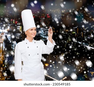 Cooking, Holidays, Advertisement And People Concept - Smiling Female Chef, Cook Or Baker With Marker Writing Something On Virtual Screen Over Snowy Night City Background