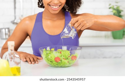 Cooking At Home. Beautiful young african woman preparing meal, pouring olive oil on vegetable salad in modern kitchen - Powered by Shutterstock