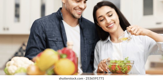 Cooking At Home. Beautiful young woman and man preparing meal, pouring olive oil on vegetable salad in modern kitchen - Powered by Shutterstock