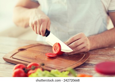 Cooking And Home Concept - Close Up Of Male Hand Cutting Tomato On Cutting Board With Sharp Knife