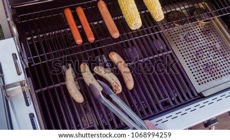 Cooking hot dogs and bratwurst on outdoor gas grill in the Summer.