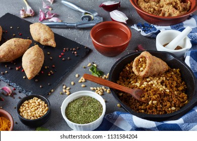 cooking a kibbeh on a kitchen of ground beef meat mixed with bulgur, fried minced meat with pine nuts, spices , garlic and herbs. ingredients in bowls on a concrete table, view from above, close-up - Shutterstock ID 1131584204