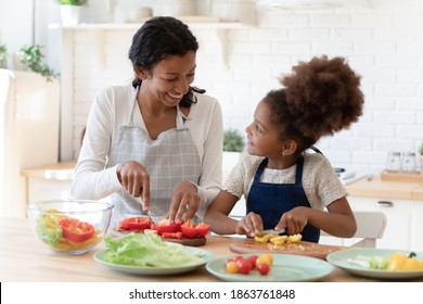 Cooking lesson. Happy patient black foster mom teaching little adopted daughter prepare healthy nutrition, single african mommy and preteen girl talking smiling engaged in useful activity at kitchen - Powered by Shutterstock