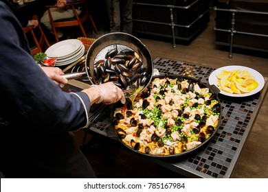 Cooking and making traditional Spanish Paella in iron cast pan. Preparing big paella, the chef adds mussels - Powered by Shutterstock