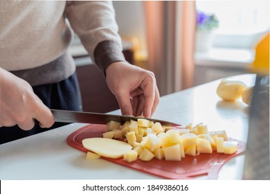 Cooking man, father, cooker. Preparation of soup, lunch, dinner in kitchen. Cutting vegetables, potatoes, carrots, onions on wooden board.Large knife.Large pot of boiling water.Surprise,help for wife