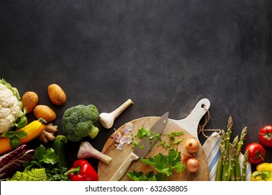 Cooking Organic Food Concept With Copy Space On Black Chalkboard Background Surface And Variety Of Fresh Ripe Vegetables Ingredients And Knife On Round Chopping Board, Overhead Studio Shot