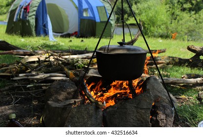 Cooking Outdoors. Cauldron On A Fire In The Forest. On The Background Of The Tent, A River And Trees.