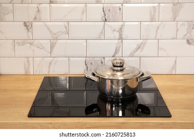 Cooking pan at modern kitchen induction cooker hob and wooden counter and white tile backsplash