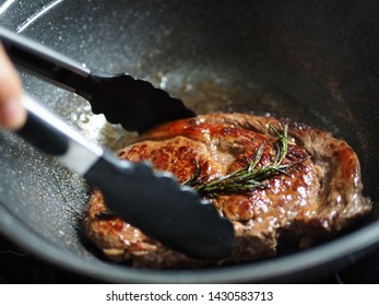 Cooking pan seared ribeye steak with rosemary in Korean granite stone coated frying pan. People enjoy home cooking lifestyle concept. (close up, selective focus, space for text)