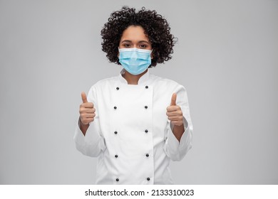 cooking, pandemic and health concept - happy smiling female chef in protective medical mask and white jacket showing thumbs up over grey background