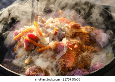 Cooking Pilaf On A Fire. Meat With Carrot Is Cooking In Cauldron On Fire With Smoke. Shallow Depth Of Field