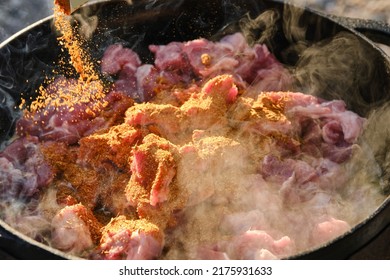 Cooking Pilaf On A Fire. Meat With Carrot And Spices Is Cooking In Cauldron On Fire With Smoke. Shallow Depth Of Field