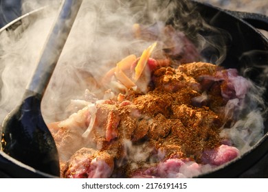 Cooking Pilaf On A Fire. Meat With Carrot And Spices Is Cooking In Cauldron On Fire With Smoke. Shallow Depth Of Field