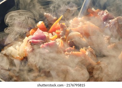 Cooking Pilaf On A Fire. Meat With Carrot Is Cooking In Cauldron On Fire With Smoke. Shallow Depth Of Field