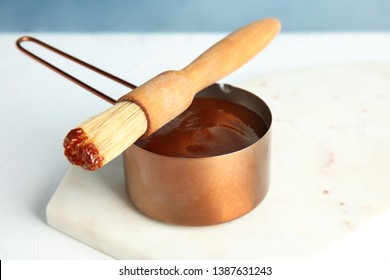 Cooking Pot With Barbecue Sauce And Brush On White Table