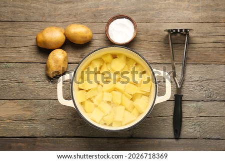 Cooking pot with boiled potatoes and masher on wooden background