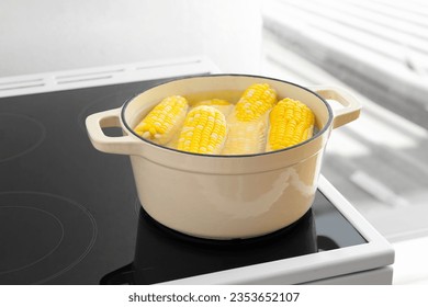 Cooking pot with boiling corn cobs on electric stove in kitchen