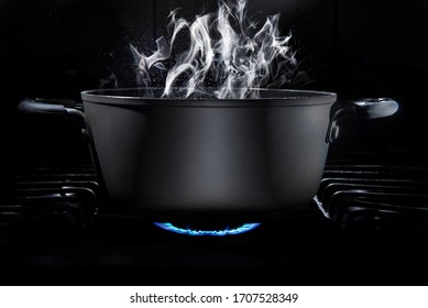 Cooking pot on stove fire with food inside in a dark kitchen and a black background with steam coming out of the cooking pot, low key light, and dark food. cooking at home or culinary school concept. 