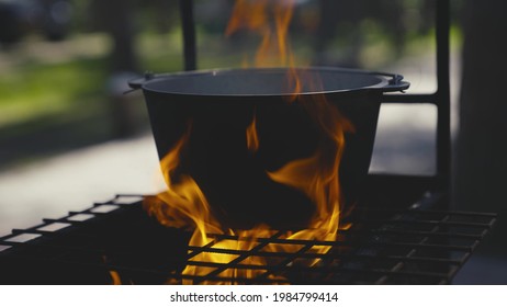Cooking pot stands on a grate with a large flame of fire, cooking outdoors in a saucepan, outdoor tourist recipes, fiery dish on weekends, relaxing in the woods