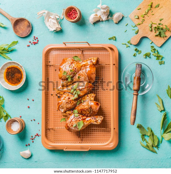 Cooking preparation of raw chicken drumsticks. Raw\
marinated Chicken legs on grill grid with ingredients,  herbs,\
spices , sauce and cooking spoon on light blue kitchen table\
background, top view