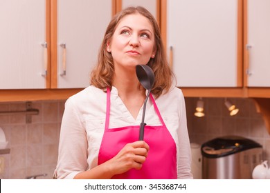 Cooking and preparing food meal concept. Thoughtful wondering and dreaming woman chef cook housewife holding ladle spoon in kitchen.