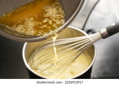 Cooking process of hollandaise sauce, pouring melted butter into the pot with egg mixture, whisking all the time at low temperature to get a creamy texture, selected focus, very narrow depth of field