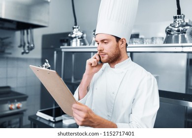 cooking, profession and people concept - male chef cook with clipboard calling on smartphone at restaurant kitchen - Powered by Shutterstock