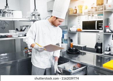 concept de cuisine, de profession et de personnes - chef masculin cuisinier avec presse-papiers faisant l'inventaire et regardant le frigo dans la cuisine du restaurant